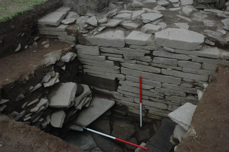 A photograph showing an excavated wall built of slab like stone up to 1.5 metres high